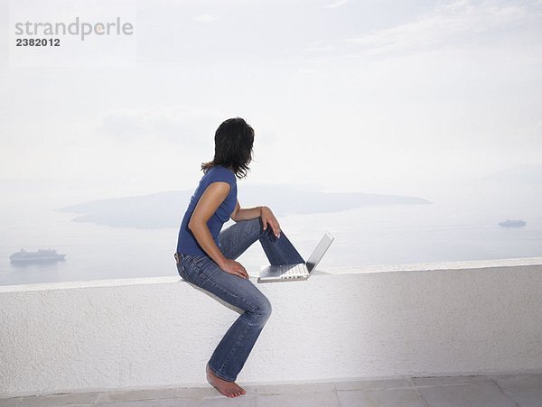 Frau mit Laptop auf einer niedrigen Wand sitzend