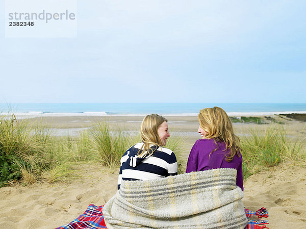 Mädchen sitzen auf Sanddüne mit Decke