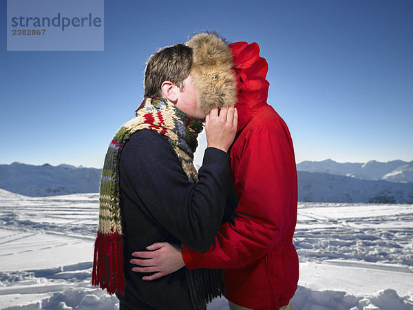 Mann küsst Frau auf Berggipfel