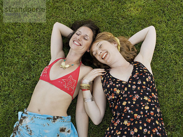 Zwei Frauen lächelnd auf Gras liegend