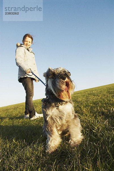 Mädchen hält Hund an der Leine auf dem Hügel