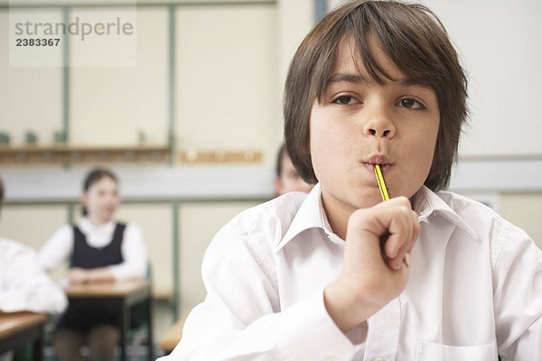 Junge mit Bleistift im Mund  im Klassenzimmer