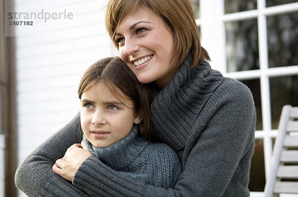 Nahaufnahme einer jungen Frau  die ihre Tochter umarmt und lächelt.