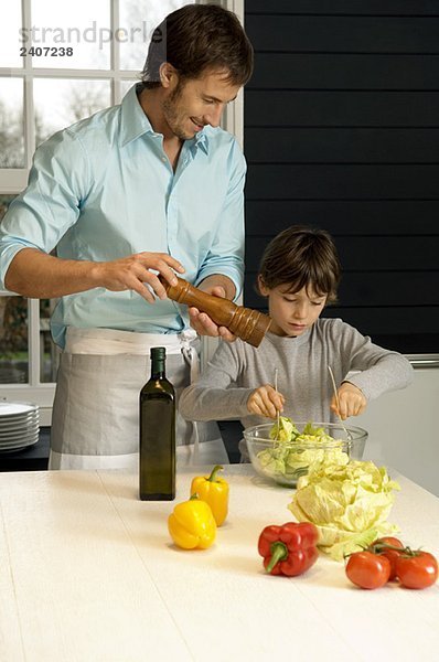Mittlerer Erwachsener  der mit seinem Sohn in der Küche das Essen zubereitet.
