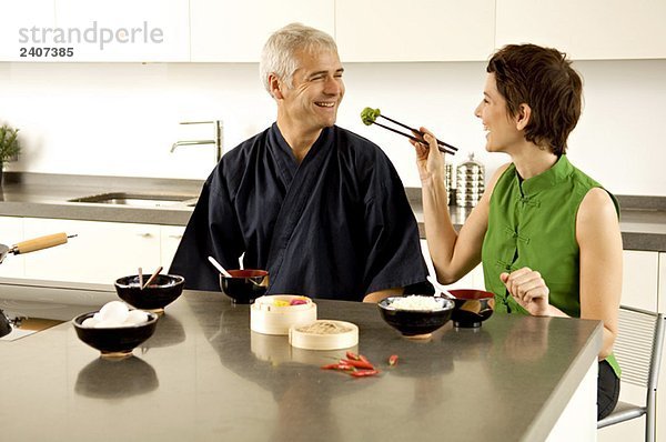 Mittlere erwachsene Frau füttert einen reifen Mann in der Küche.