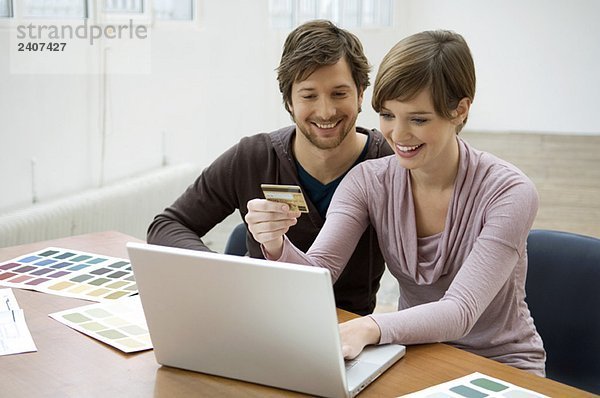 Mittlerer Erwachsener Mann und eine junge Frau  die einen Laptop benutzen und eine Kreditkarte haben.