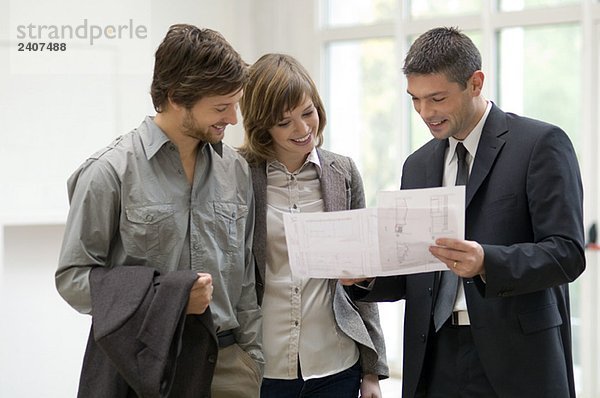 Immobilienmakler  der einem Paar einen Plan zeigt.