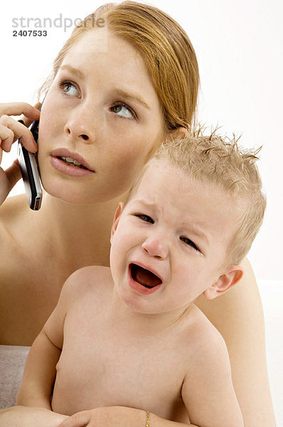 Nahaufnahme einer jungen Frau  die auf einem Handy spricht und einen weinenden Jungen hält.