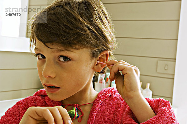 Porträt eines Jungen  der sein Ohr mit einem Wattestäbchen putzt.