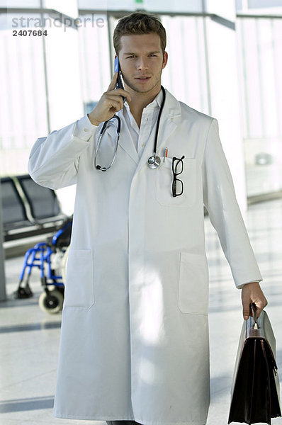 Ein männlicher Arzt hält eine Tasche und spricht auf einem Handy.