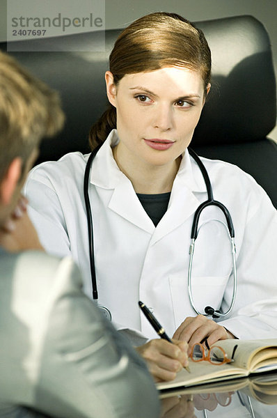 Ärztin sitzt am Schreibtisch und spricht mit einem Patienten