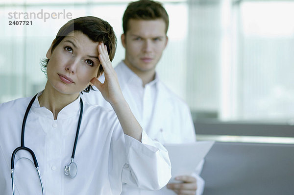 Eine Ärztin sieht besorgt aus  ein Mann steht hinter ihr.