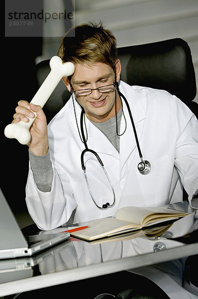 Nahaufnahme eines männlichen Arztes  der an einem Schreibtisch sitzt und einen Knochen hält.