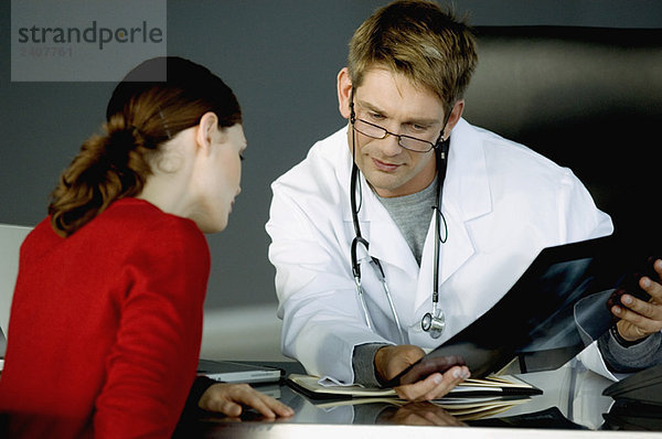 Männlicher Arzt  der einer Patientin einen Röntgenbericht zeigt.