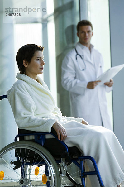 Patientin im Rollstuhl und Arzt im Hintergrund