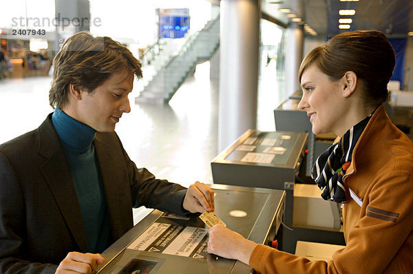 Geschäftsmann mit weiblicher Check-in-Betreuerin am Flughafen-Check-in-Schalter