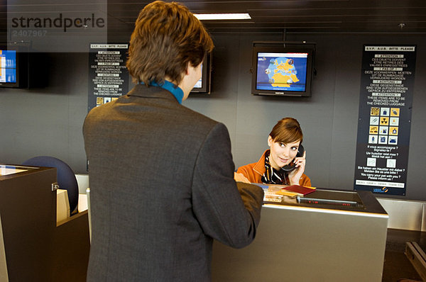Rückansicht eines Geschäftsmannes am Flughafen-Check-in-Schalter und der Check-in-Betreuer am Telefon
