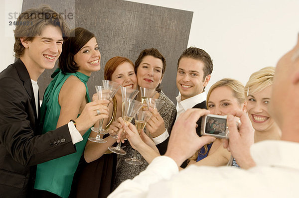 Ein reifer Mann fotografiert eine Gruppe von Leuten  die mit Weingläsern auf einer Party anstoßen.