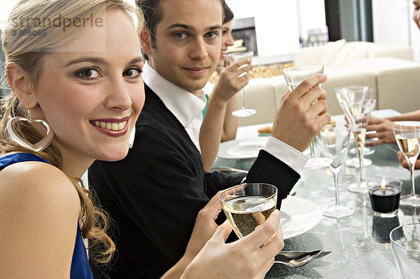 Porträt eines jungen Paares  das bei einer Dinnerparty mit Freunden ein Glas Champagner hält