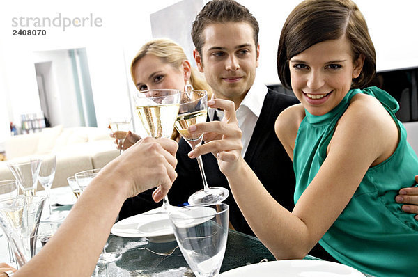 Porträt einer jungen Frau  die auf einer Dinnerparty mit Champagner anstößt.