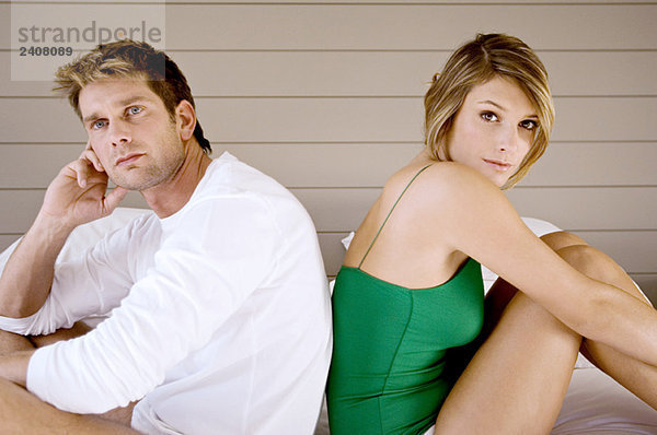 Seitenprofil eines mittelgroßen Mannes und einer jungen Frau  die Rücken an Rücken auf dem Bett sitzen.