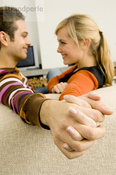 Seitenprofil eines jungen Paares  das auf einer Couch sitzt und sich gegenseitig die Hände hält.