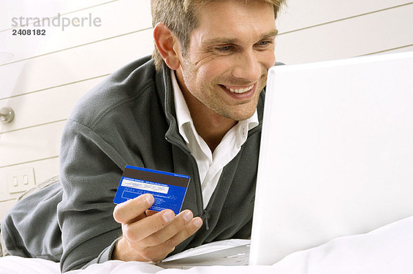 Mittlerer erwachsener Mann  der an einem Laptop arbeitet und eine Kreditkarte hält.