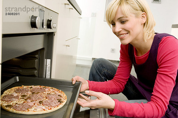 Junge Frau  die ein Tablett mit Pizza in den Ofen stellt.