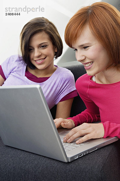 Zwei junge Frauen  die einen Laptop benutzen und lächeln.