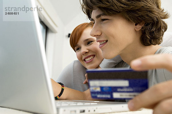 Nahaufnahme eines Teenagers mit Kreditkarte und Laptop mit einer jungen Frau neben ihm