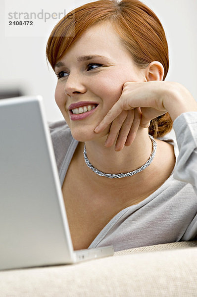 Nahaufnahme einer jungen Frau vor einem Laptop sitzend und lächelnd