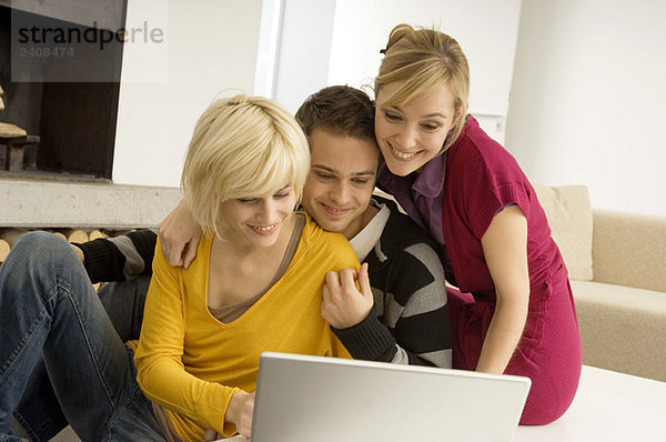 Junger Mann mit zwei jungen Frauen  die auf einen Laptop schauen und lächeln.