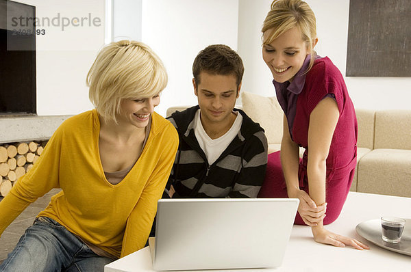 Junger Mann mit zwei jungen Frauen beim Blick auf einen Laptop