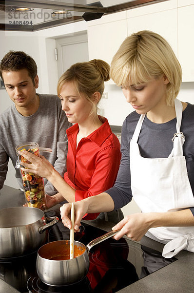 Zwei junge Frauen und ein junger Mann bei der Zubereitung des Essens in der Küche