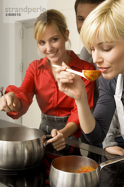 Zwei junge Frauen und ein junger Mann bei der Zubereitung des Essens in der Küche