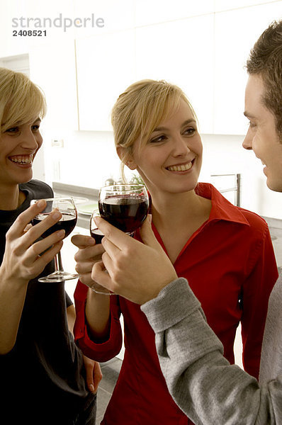 Zwei junge Frauen und ein junger Mann stoßen mit Weingläsern an.