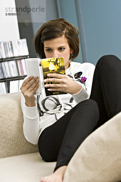 Junge Frau sitzt auf einer Couch und liest ein Buch.