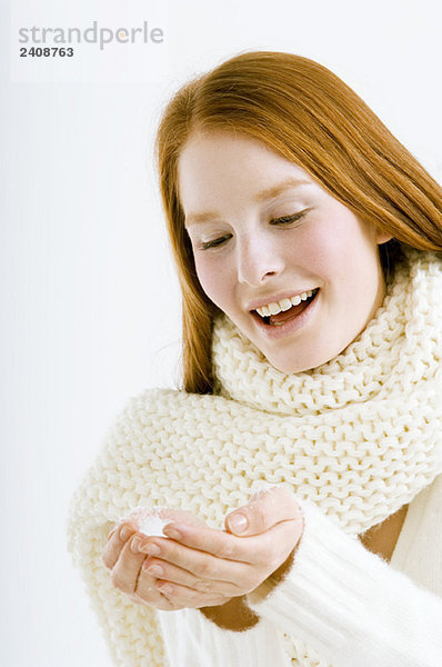 Nahaufnahme einer jungen Frau  die Schnee in hohlen Händen hält und lächelt.