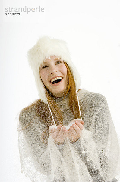 Junge Frau hält Schnee in ihren hohlen Händen und lächelt
