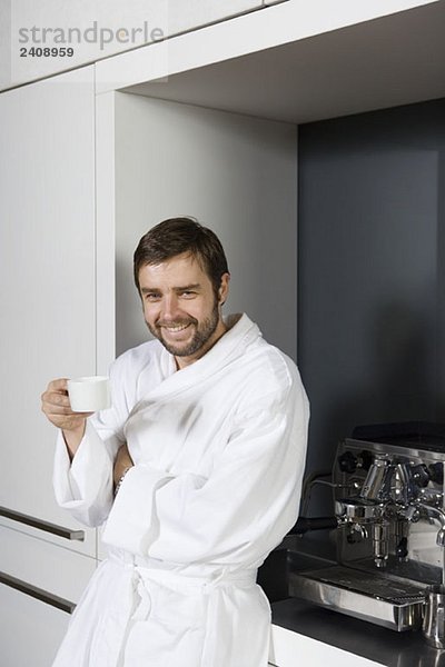 Ein lächelnder Mann im Bademantel mit einer Kaffeetasse.