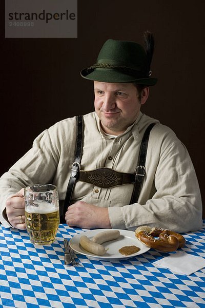 Stereotypischer deutscher Mann in bayerischer Tracht mit Bier und deutschem Essen
