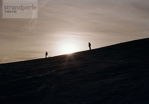 Zwei Skifahrer auf einer Bergseite bei Sonnenuntergang