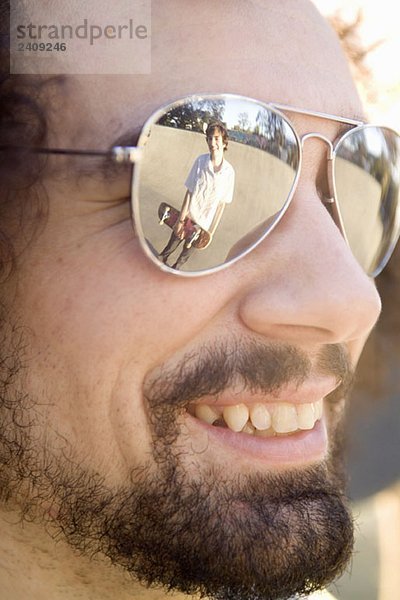 Ein Skateboarder  der sich in der Sonnenbrille eines Freundes spiegelt.