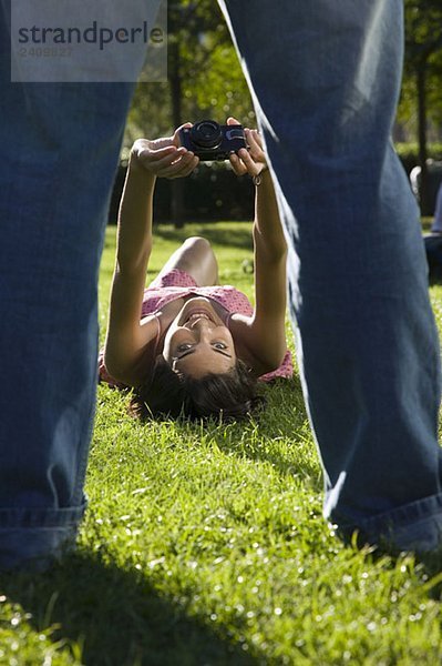 Eine junge Frau  die auf Gras liegt und einen Mann fotografiert.