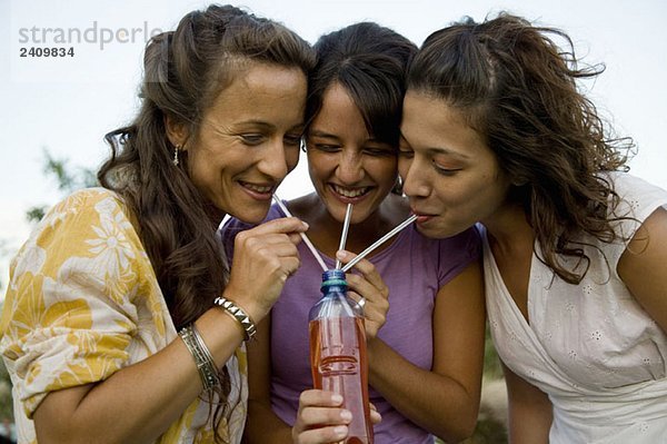 Drei Frauen  die durch Strohhalme aus einer Flasche trinken.