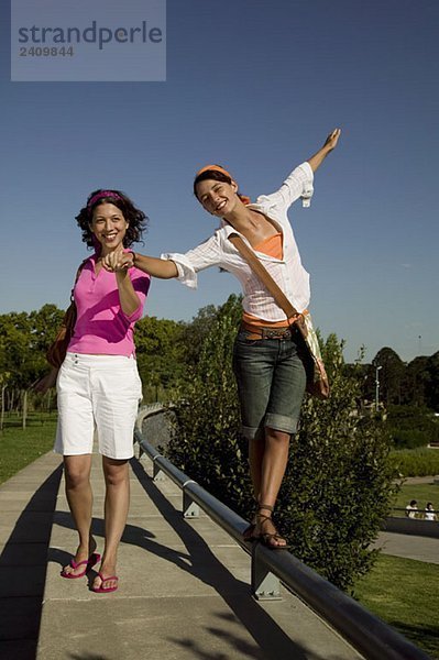 Zwei junge Frauen  die auf einer Mauer laufen und Händchen halten.