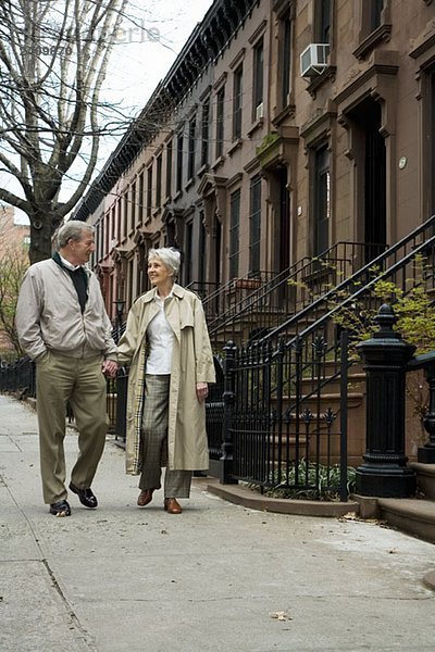 Ein älteres Paar  das auf dem Bürgersteig der Stadt spazieren geht.