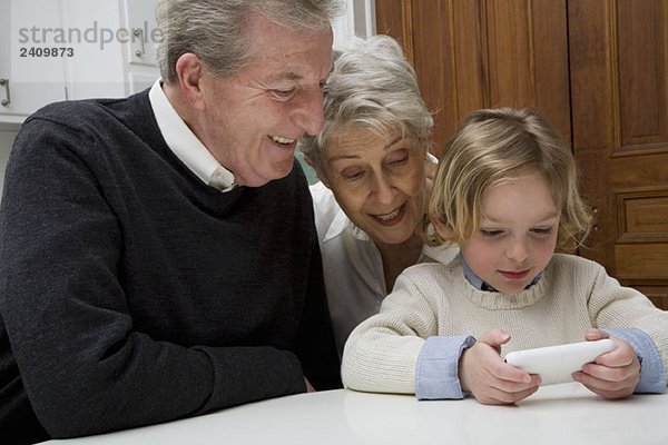Ein Enkel  der ein elektronisches Gerät benutzt  während seine Großeltern zusehen.