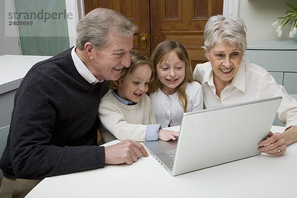Enkelkinder  die einen Laptop benutzen  während ihre Großeltern zusehen.