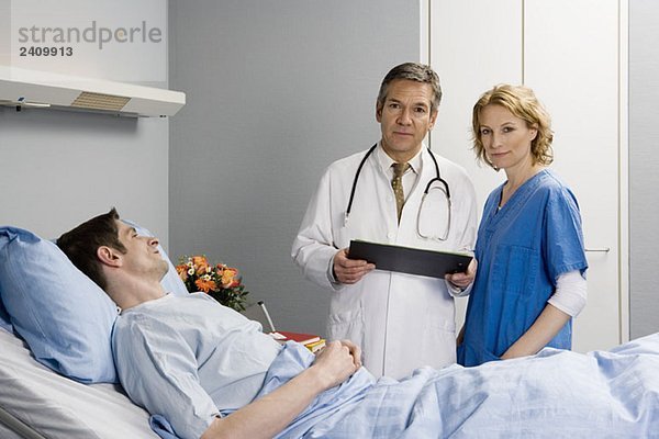 Zwei Mitarbeiter des Gesundheitswesens stehen neben einem Patienten im Bett.